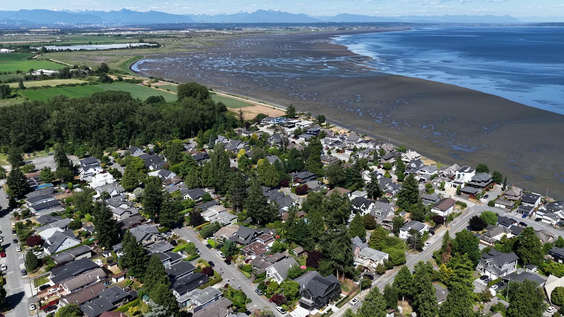 Drone view of a waterfront neighbourhood and the tidal flats, with the mountains behind